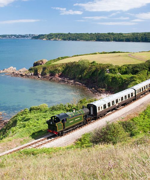 Linha de trem costeira passando por Churston, com vista para o mar e falésias verdes no sul da Inglaterra